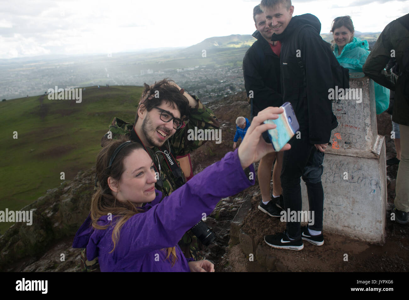 A couple do a selfie on top of the peak. The peak of King Arthur's Seat is a popular destination for both locals and tourists. The peak and souronding Stock Photo
