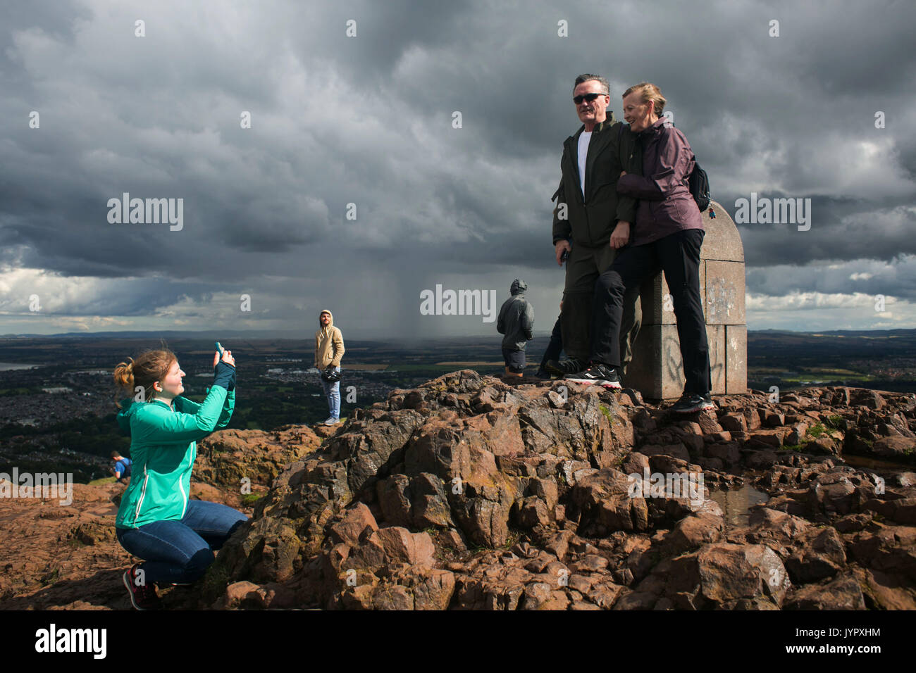 A couple have their phot taken on top of thepeak. Rain is over Edinburgh and coming closer. The peak of King Arthur's Seat is a popular destination fo Stock Photo