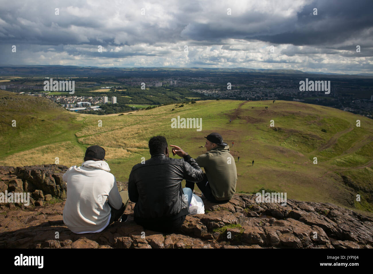 Three friends relax over beer on top of the peak. The peak of King Arthur's Seat is a popular destination for both locals and tourists. The peak and s Stock Photo