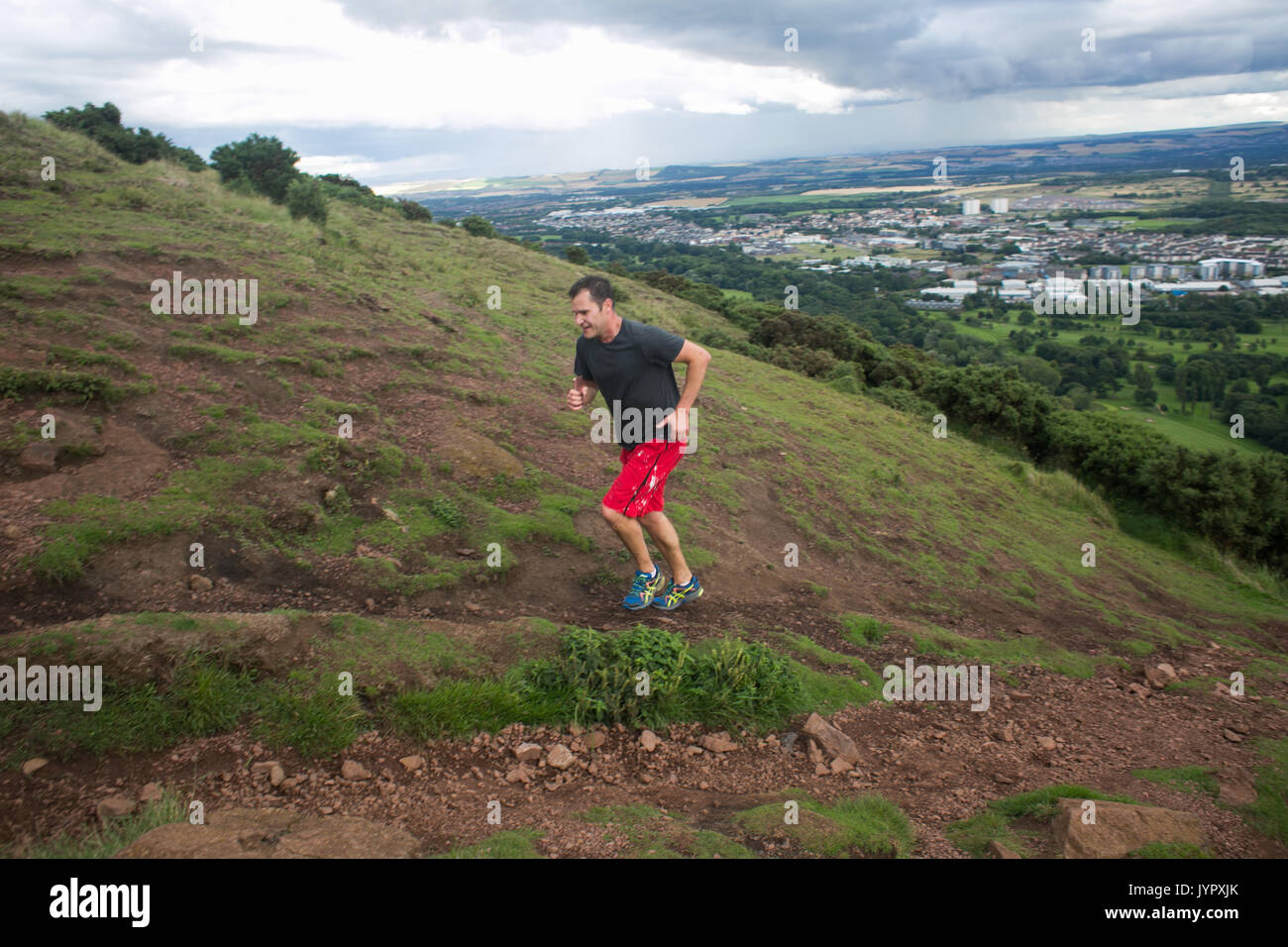 A runner makes his way to the peak. The peak of King Arthur's Seat is a popular destination for both locals and tourists. The peak and surrounding roc Stock Photo