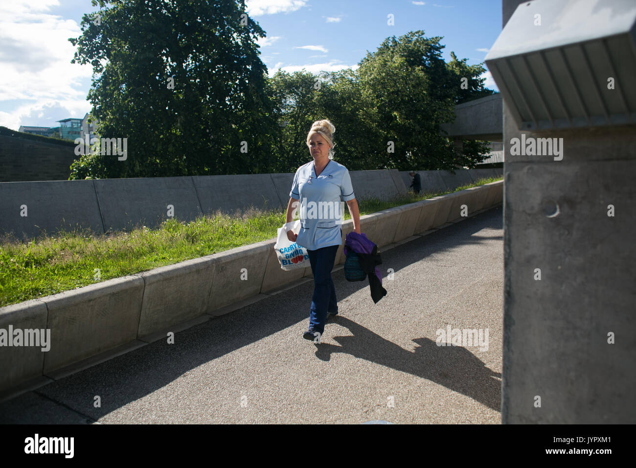 An NHS nurse walk along the concrete walk way behind the Scottish Parliament. Stock Photo