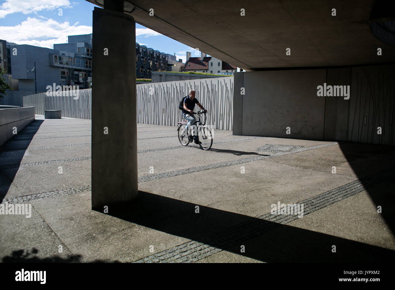 A bike rider rides his bike along the concrete walk way near the Scottish Parliament. Stock Photo
