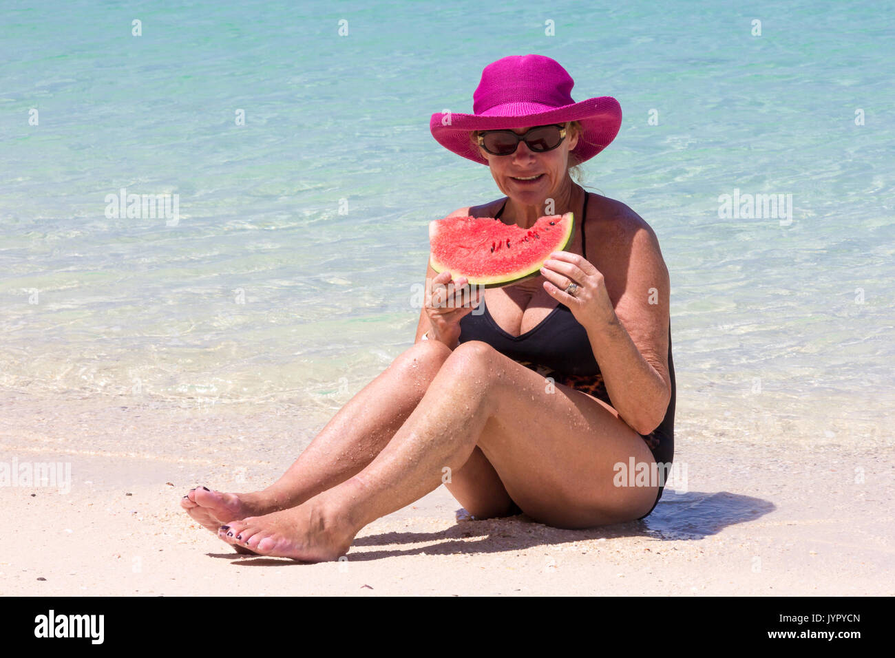 Senior woman wearing pink hat with water melon sitting in sea, Koh Lao Liang, Trang, Thailand Stock Photo