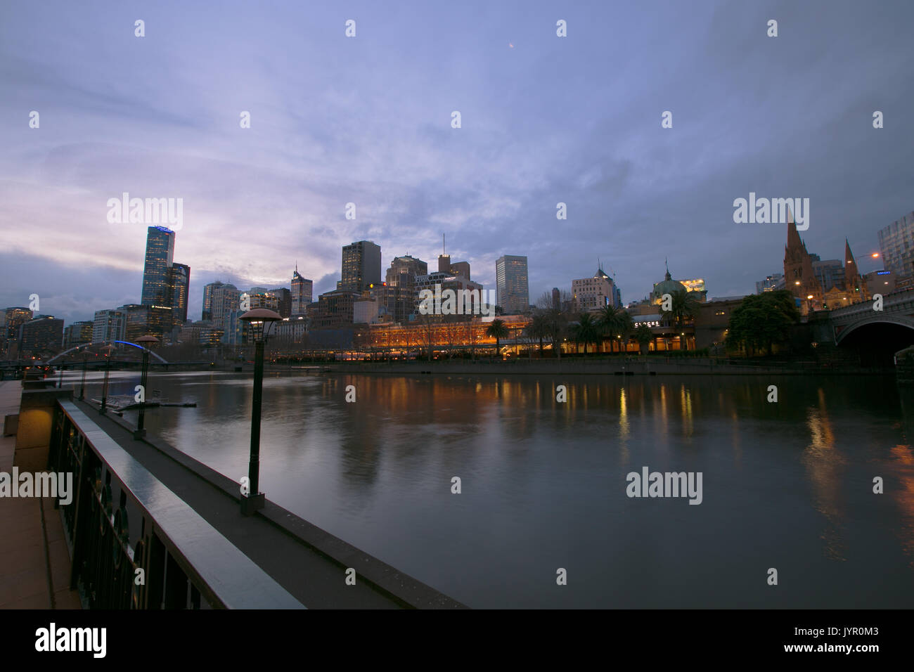 A long exposure photo of the Yarra River, Flinders Street Station, a cluster of buildings, and  the Southbank Footbridge. Stock Photo