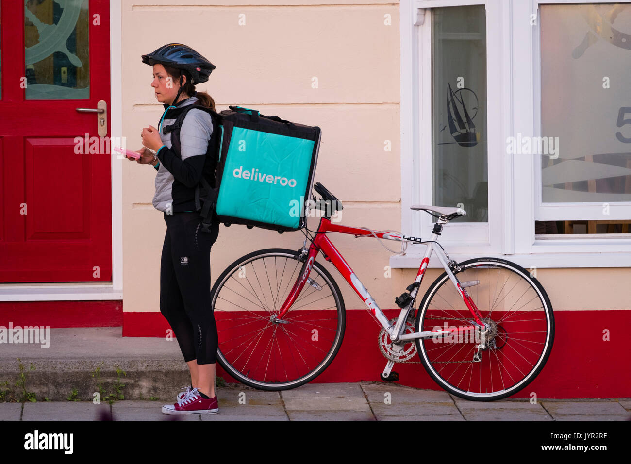 The Gig Economy in the UK: A young self-employed woman girl with her bicycle working for Deliveroo, the take-away food delivery company Stock Photo