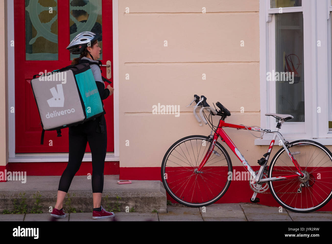 The Gig Economy in the UK: A young self-employed woman girl with her bicycle working for Deliveroo, the take-away food delivery company Stock Photo