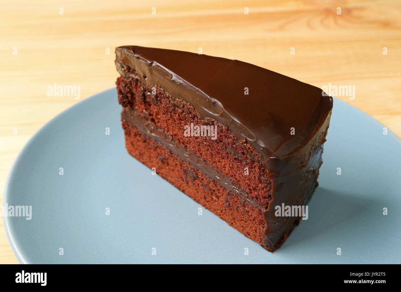 Piece of Delectable Chocolate Layer Cake Served on Blue Plate on the Wooden Table Stock Photo