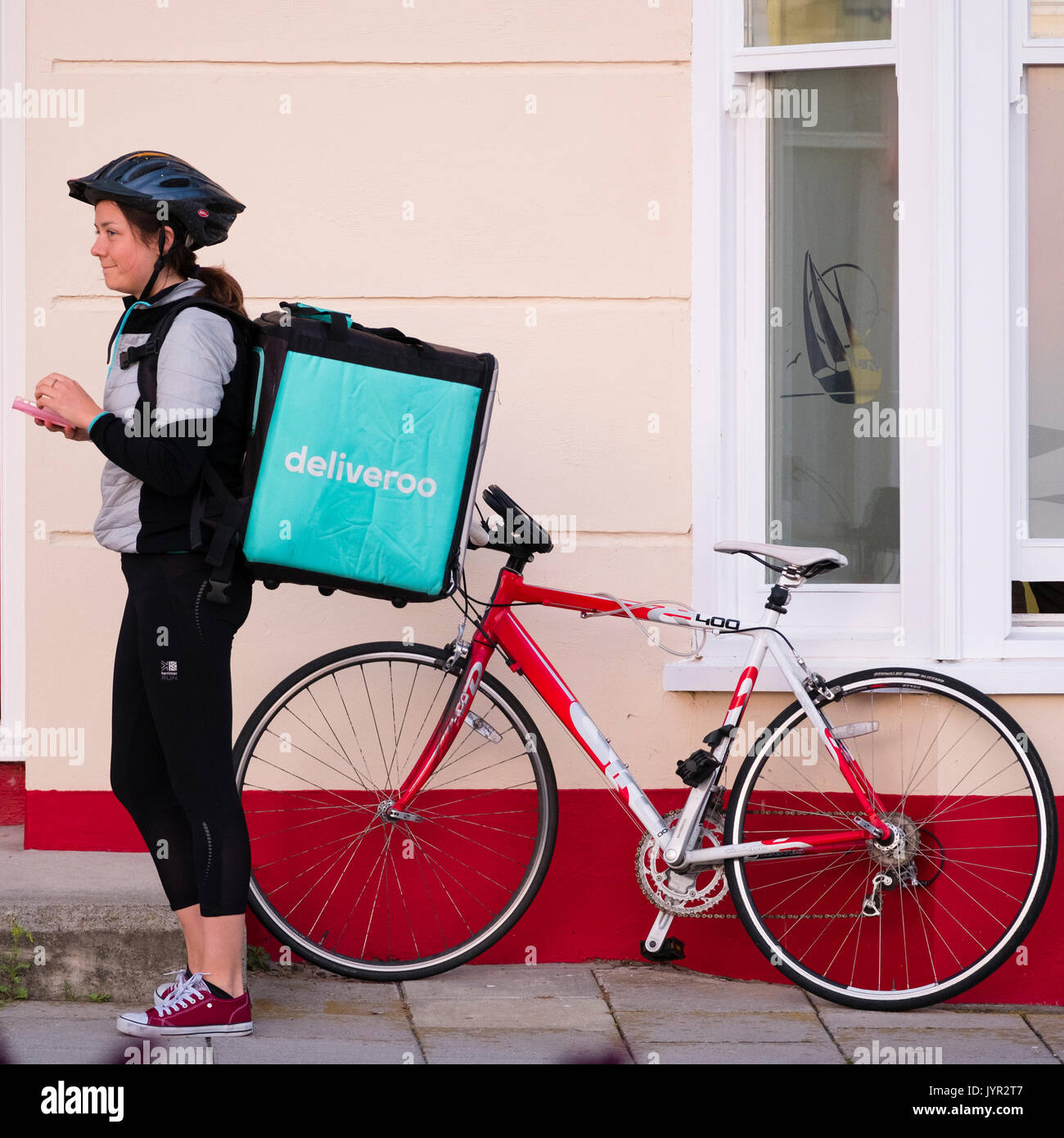 The Gig Economy in the UK: A young self-employed woman girl with her bicycle working for Deliveroo, the take-away food delivery company Stock Photo