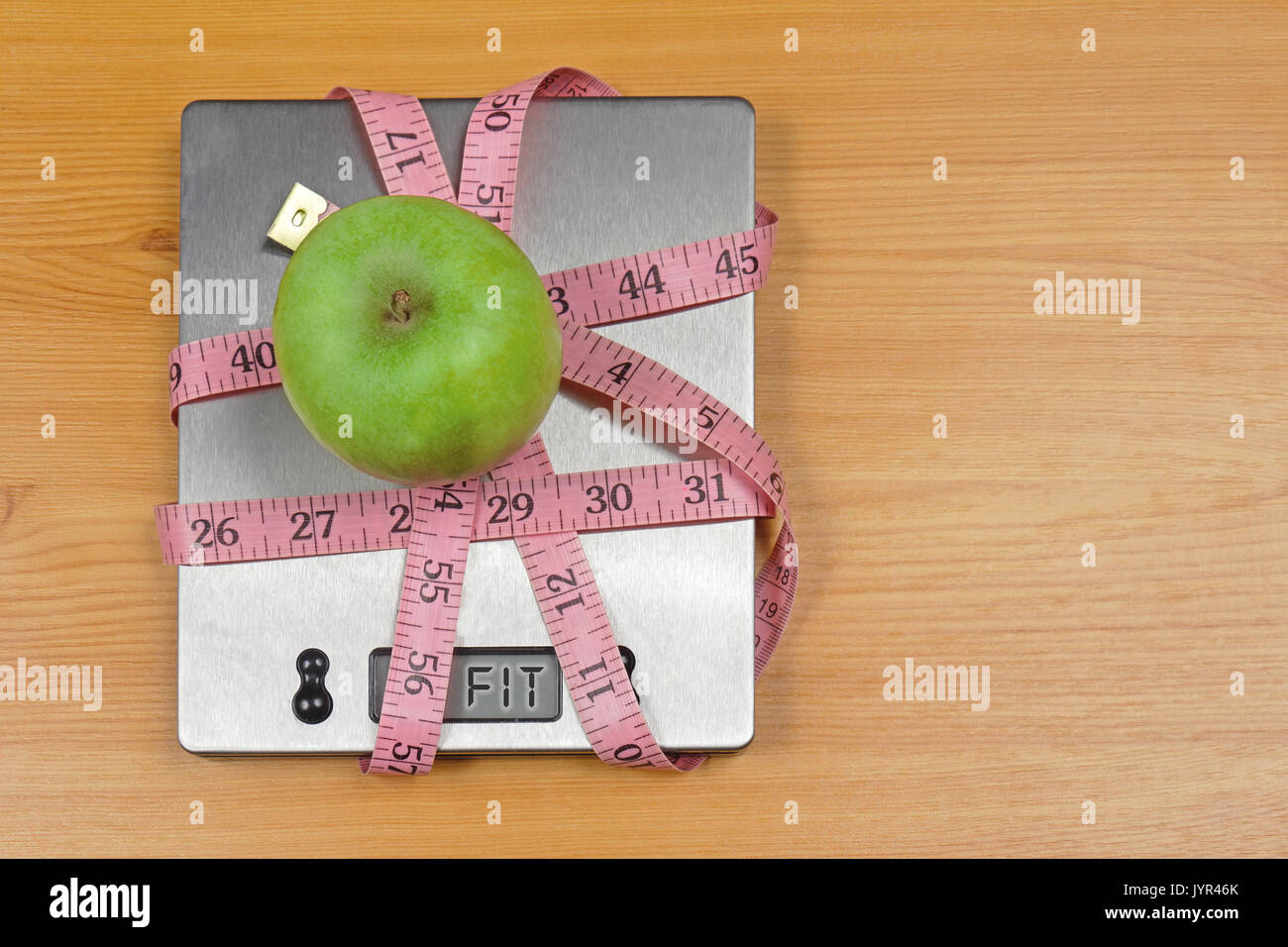 Green apple on digital kitchen scale wrapped in tape measure with fit sign on display Stock Photo