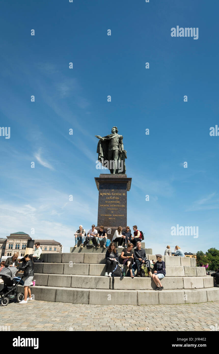 People sitting on the steps of a bronze statue of King Gustav III in Stockholm, Sweden on a sunny day Stock Photo