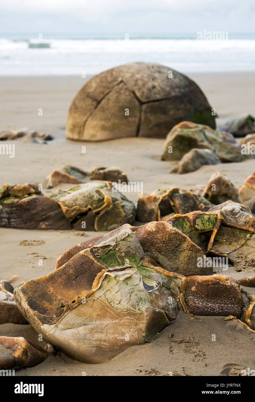 Shattered Moeraki Boulders with another intact boulder in the background Stock Photo