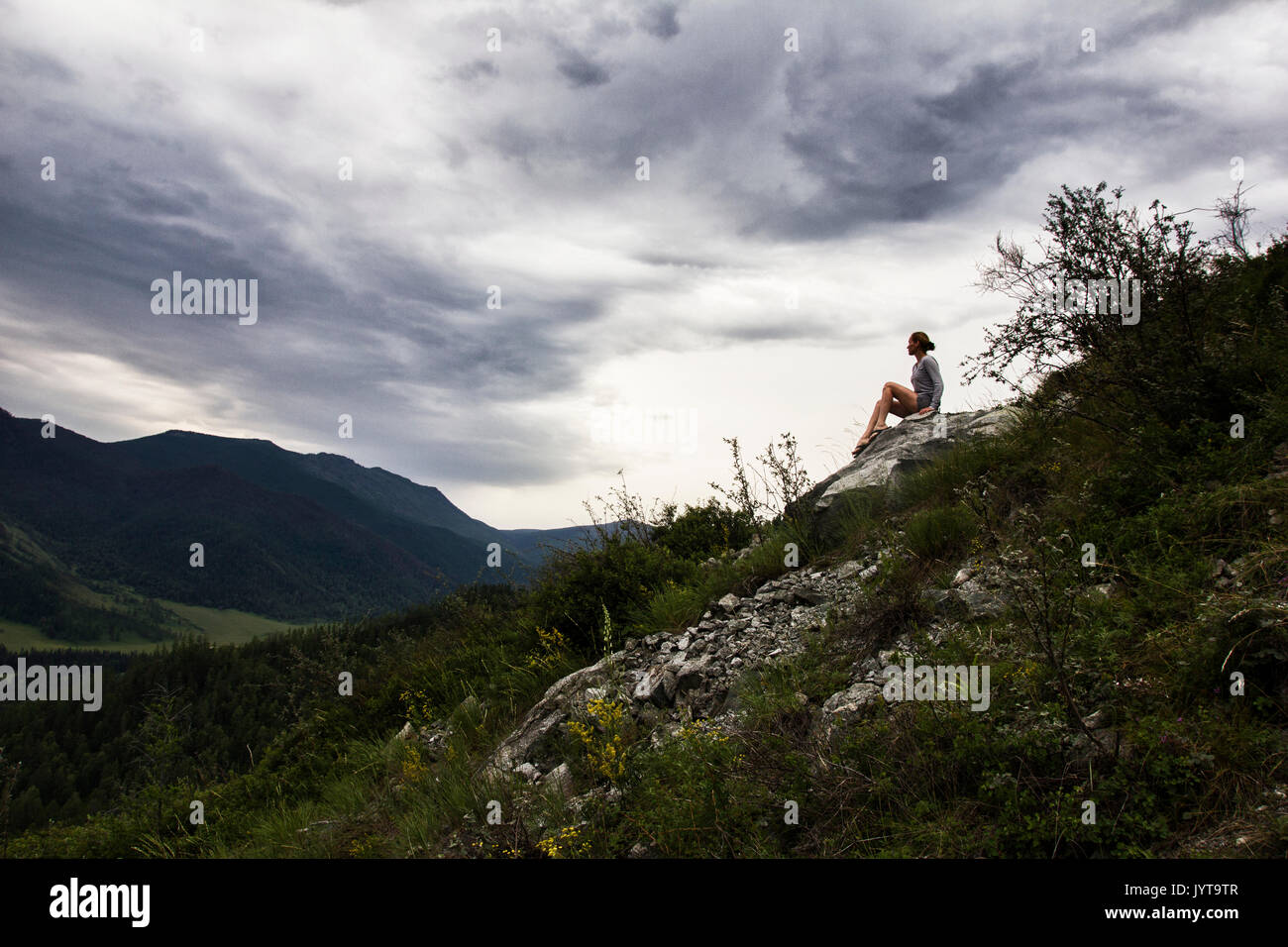 Beautiful woman sitting on mountain top and contemplating the sky clouds Stock Photo