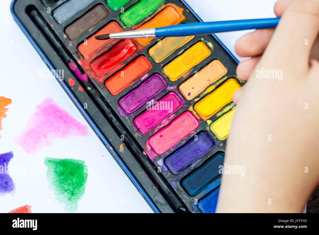 Child Painting With Watercolor Paints on a White Paper Book In Natural Light Stock Photo