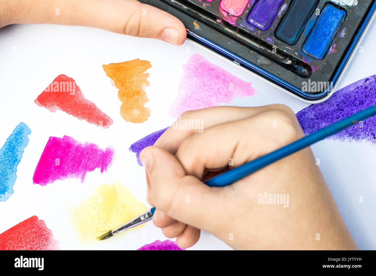 Child Painting With Watercolor Paints on a White Paper Book In Natural Light Stock Photo