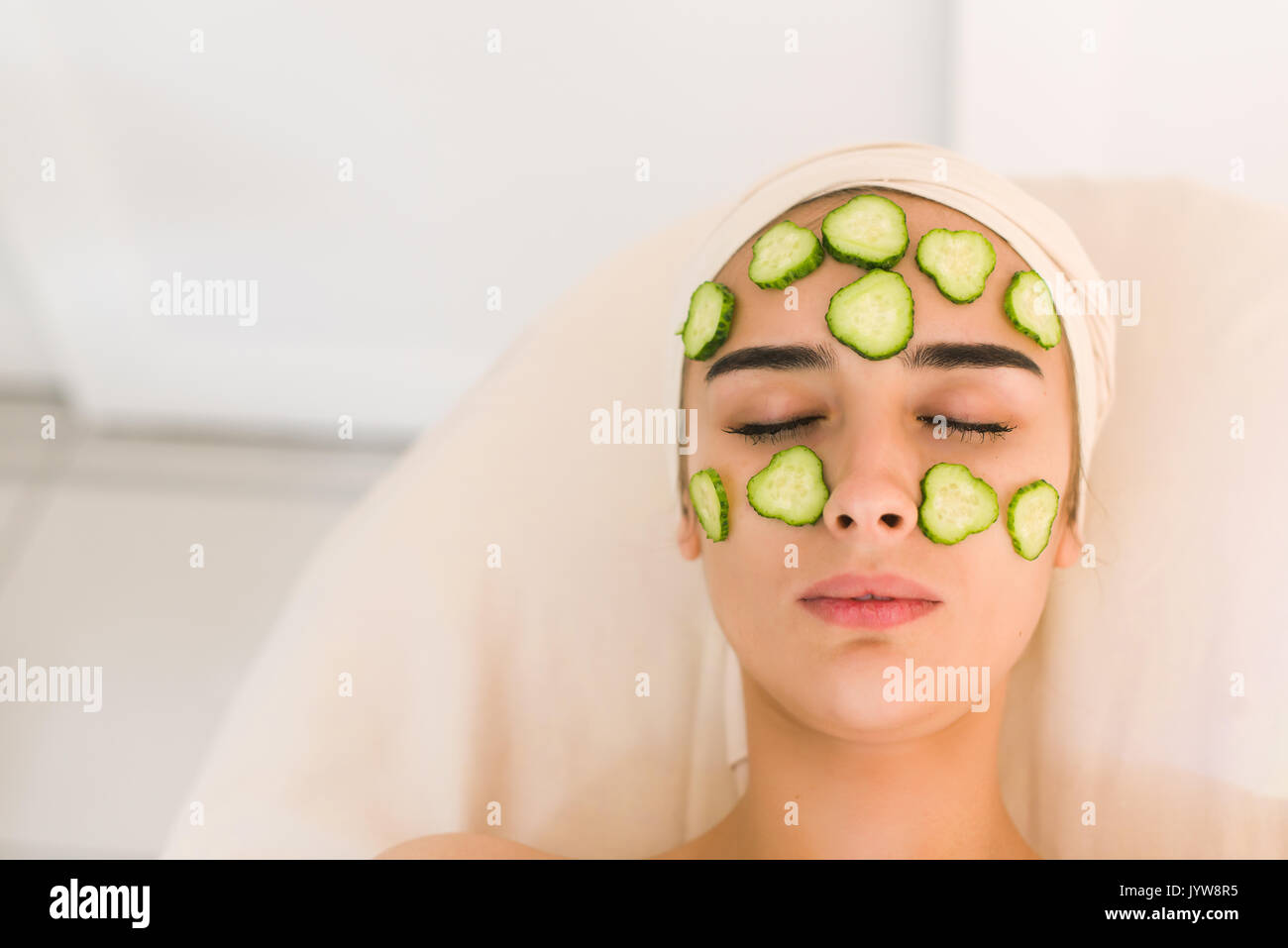 Cucumber slices on eyes. Young woman with facial mask of cucumber in beauty salon. Girl with closed eyes with a mask of cucumbers on her face. Stock Photo