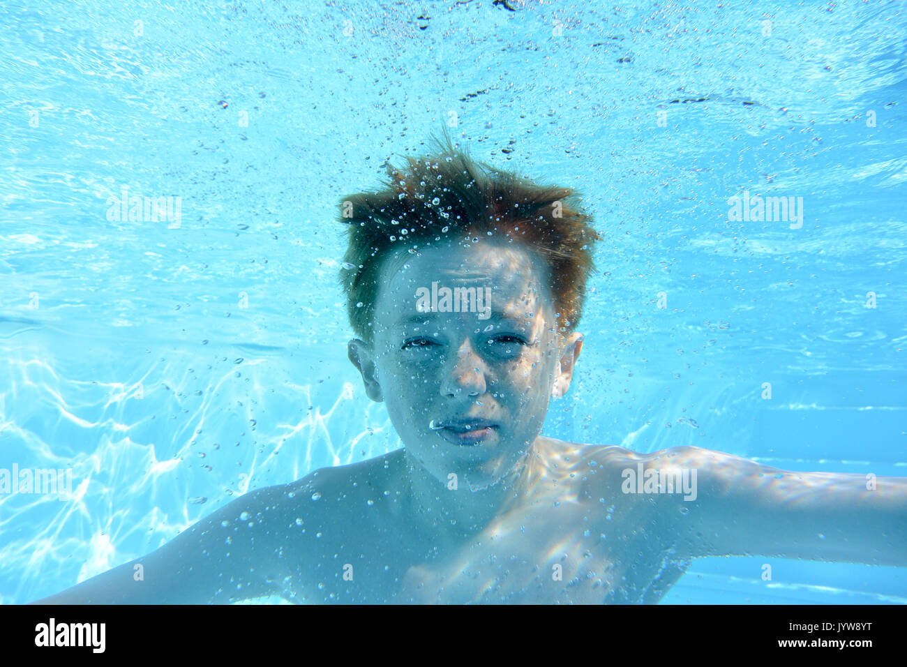 Auburn haired teenage boy, underwater in a swimming pool, looking into camera Stock Photo