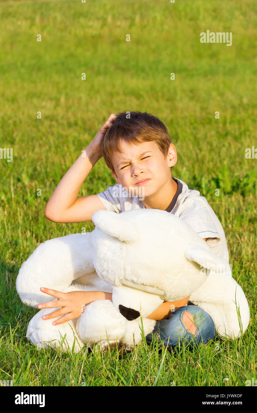Boy sitting on the grass with teddy bear and planning or thinking about ...