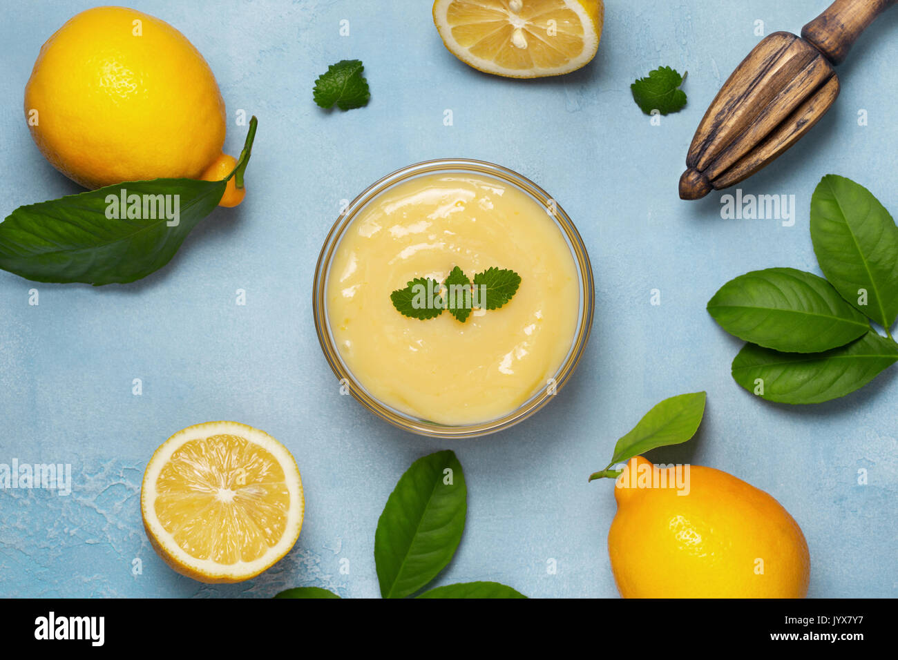 lemon curd in a glass bowl, fresh lemons, juicer on a blue background Stock Photo
