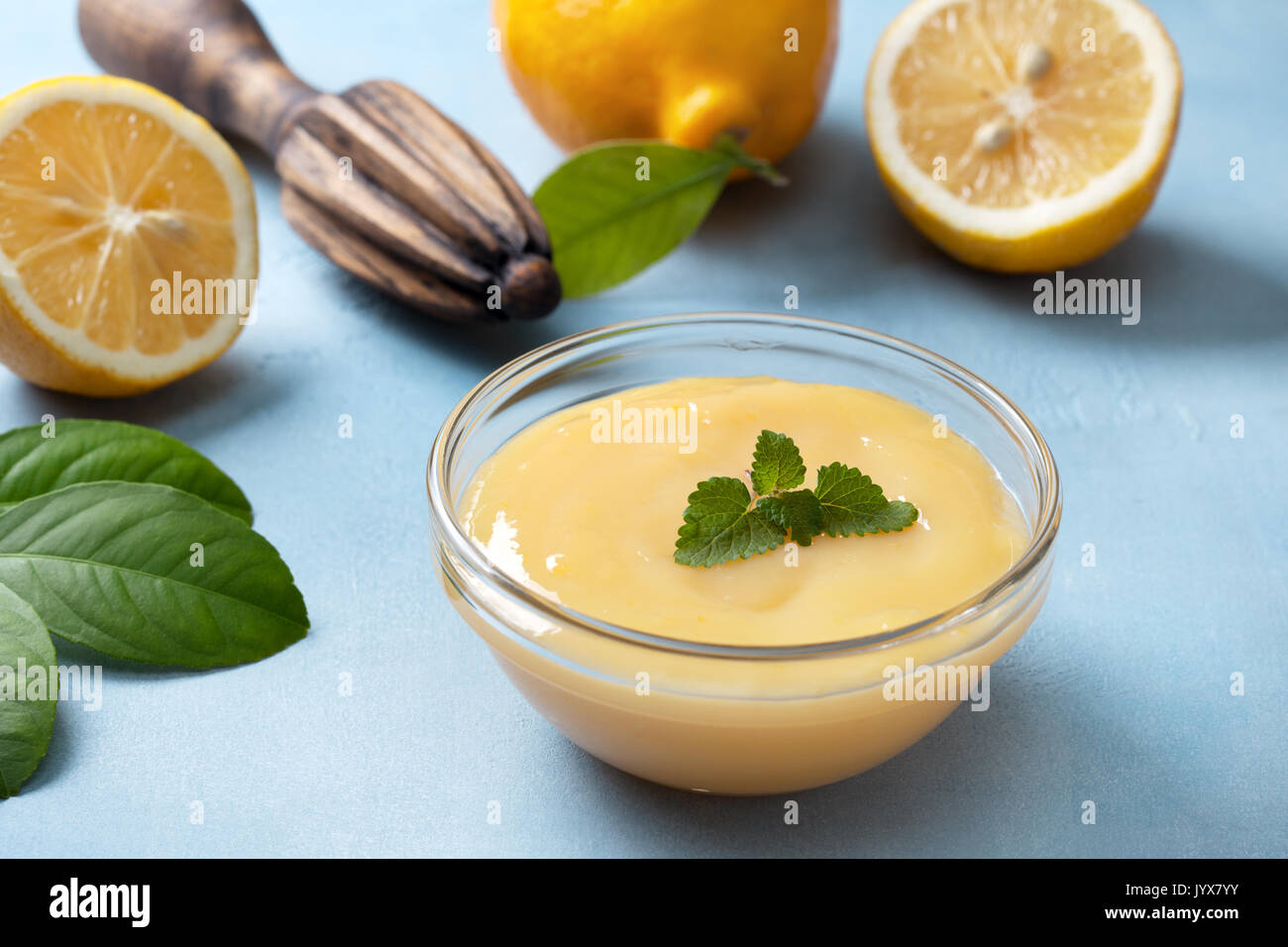 lemon curd in a glass bowl, fresh lemons, juicer on a blue background Stock Photo