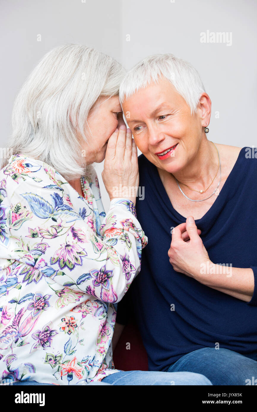 Two older women whispering Stock Photo