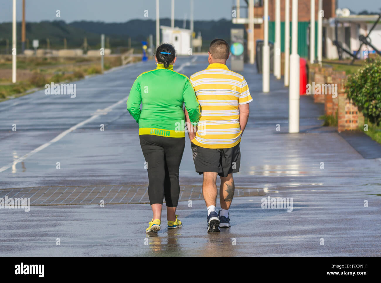 Couple walking in the rain along an otherwise deserted seafront promenade. Stock Photo
