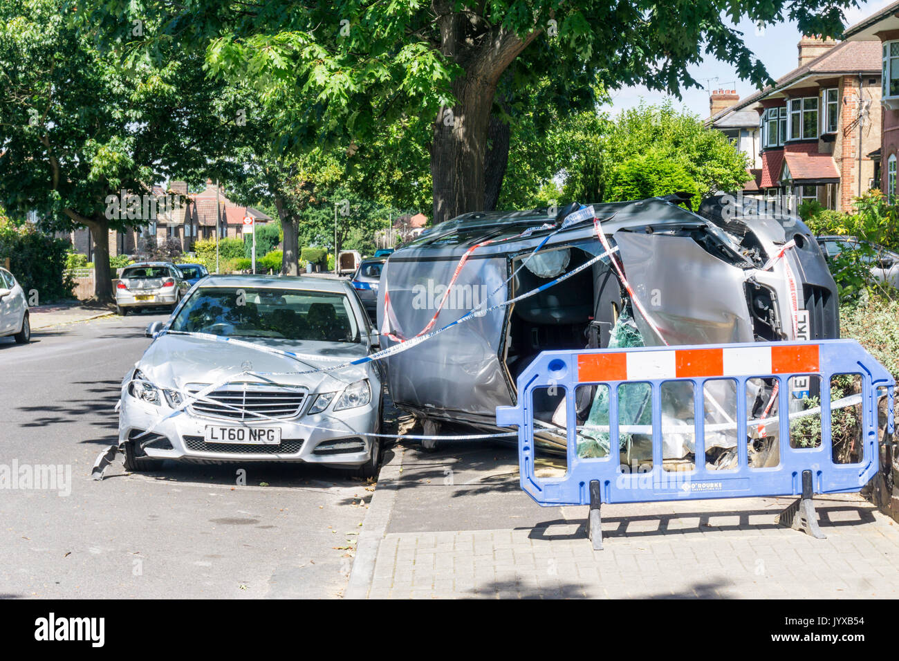 Result of traffic accident in suburban residential road.  Silver Nissan Qashqai Visia car overturned onto side on pavement & covered with police tape. Stock Photo