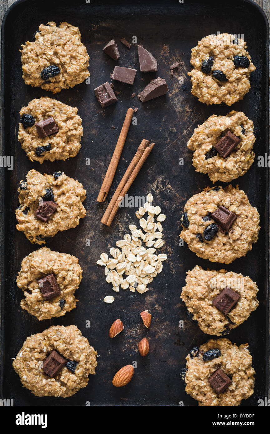 Top view of freshly baked oatmeal raisin cookies with dark chocolate, cinnamon and nuts on old rusty cookies sheet. Stock Photo