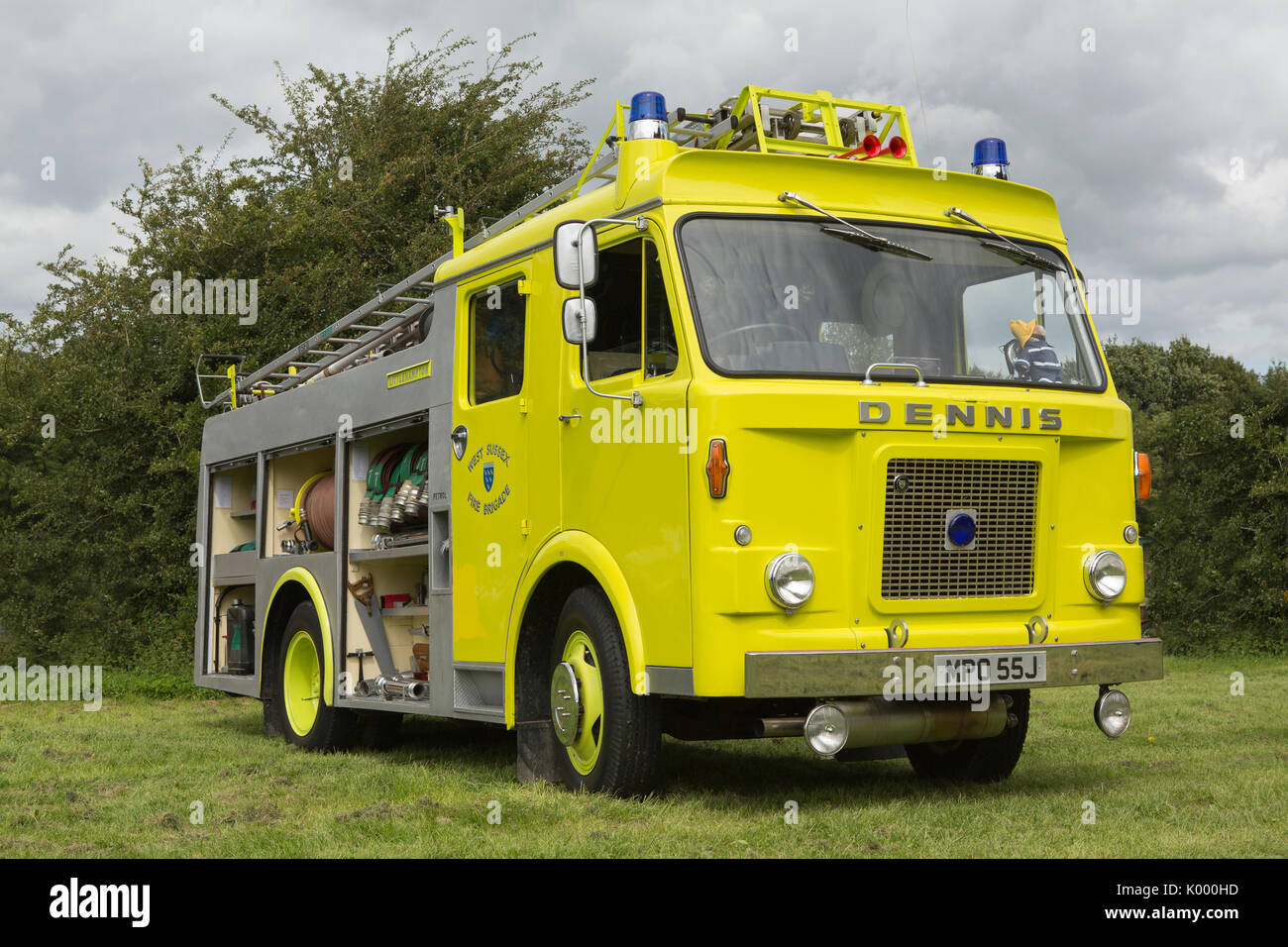1970 Vintage Dennis fire appliance in yellow livery stationary in a rural setting. Side shutters open showing the preserved fire fighting equipment. Stock Photo