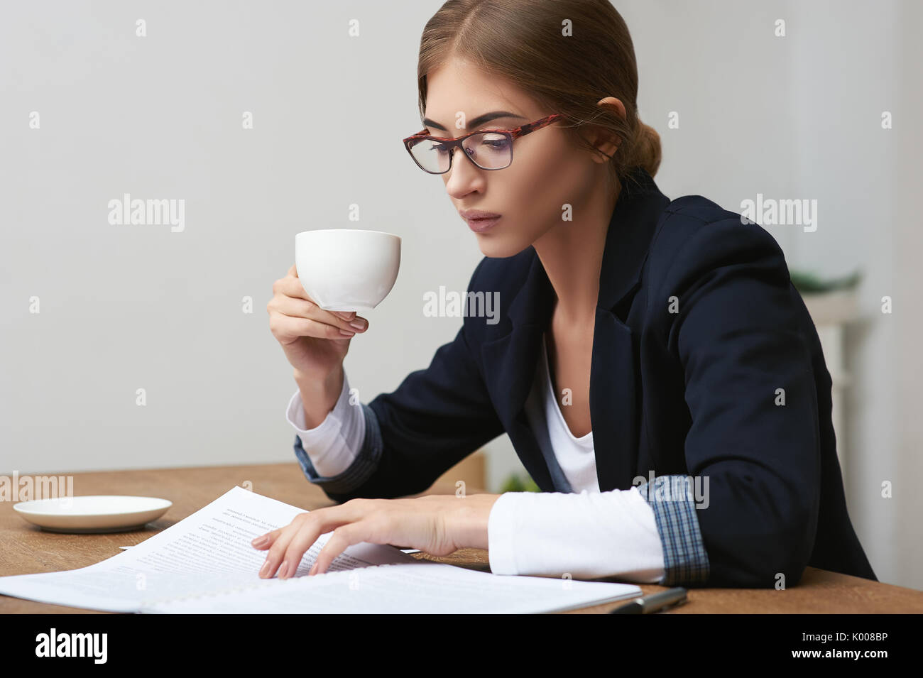 Pretty business woman reading data documents sitting at the table in office and drinking coffee Stock Photo