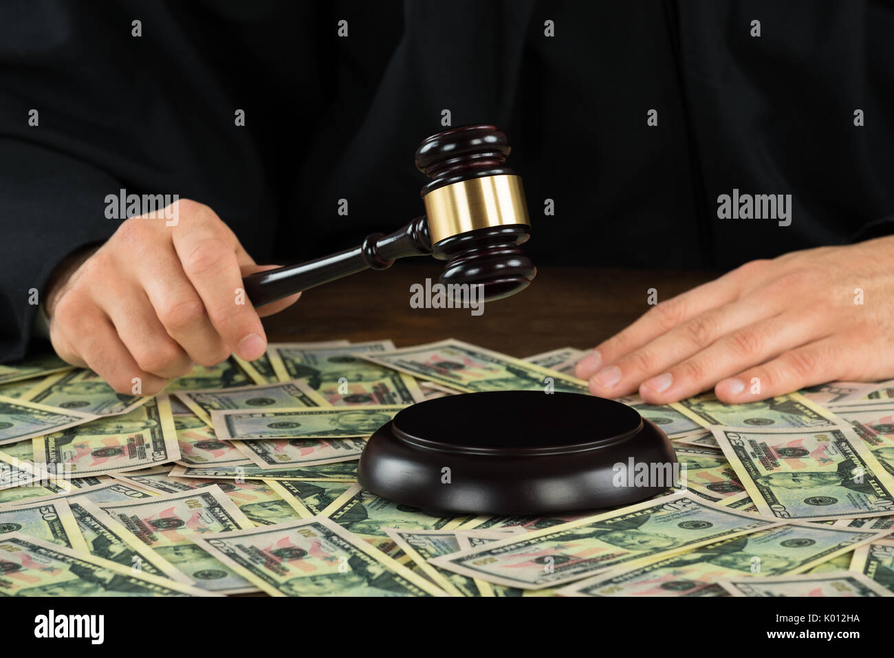 Midsection of corrupt judge hitting gavel with banknotes spread at desk in courtroom Stock Photo