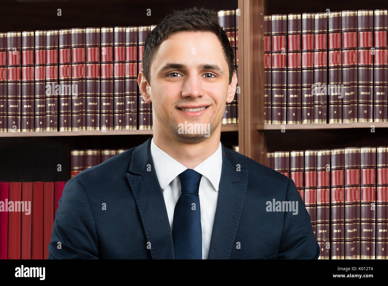 Portrait of confident male lawyer standing arms crossed against bookshelf in courtroom Stock Photo