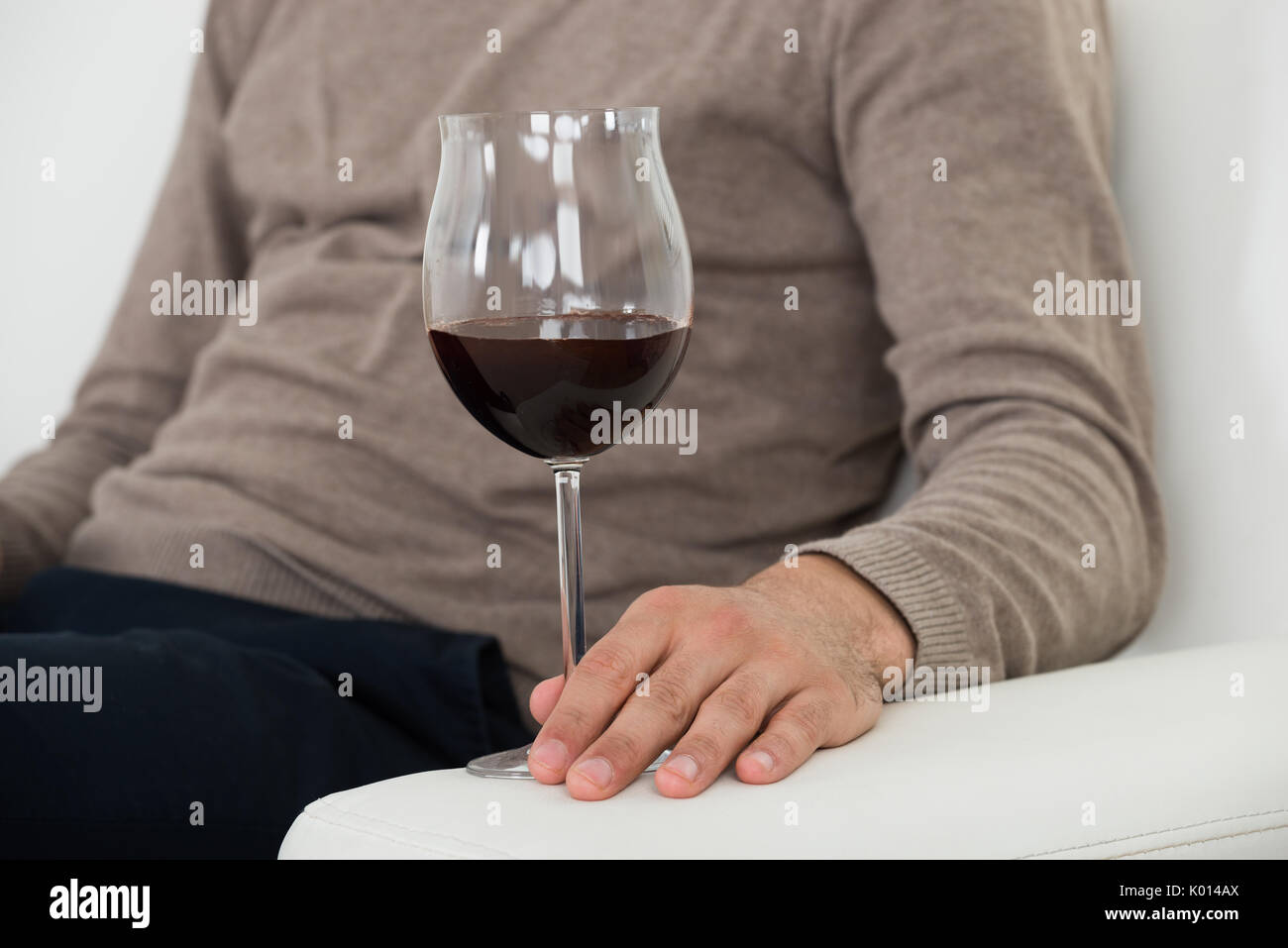 Midsection of man holding red wineglass while sitting on sofa at home Stock Photo