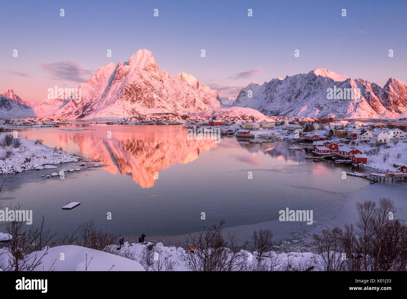 Snowy peaks are reflected in the frozen sea at sunset Reine Bay Nordland Lofoten Islands Norway Europe Stock Photo