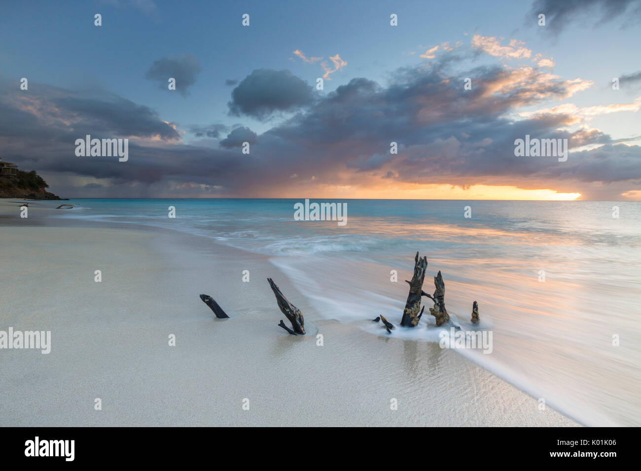 The waves and caribbean sunset frames tree trunks on Ffryers Beach Antigua and Barbuda Leeward Islands West Indies Stock Photo