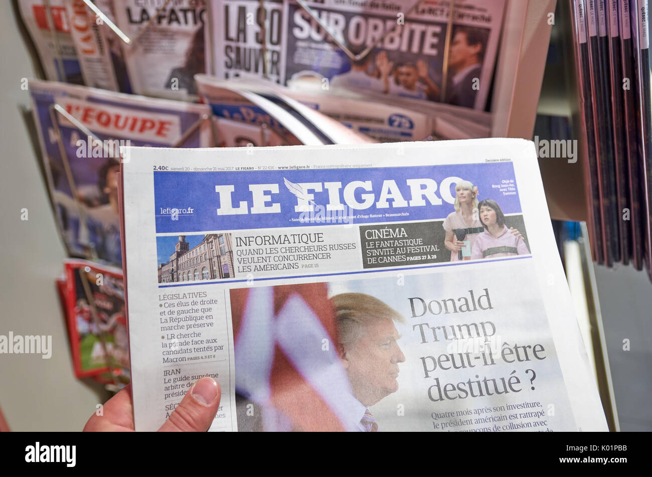 LONDON, ENGLAND - MAY 14, 2017 : A hand holding Le Figaro newspaper over newsstand background in Paris. Le Figaro is a French daily morning newspaper  Stock Photo