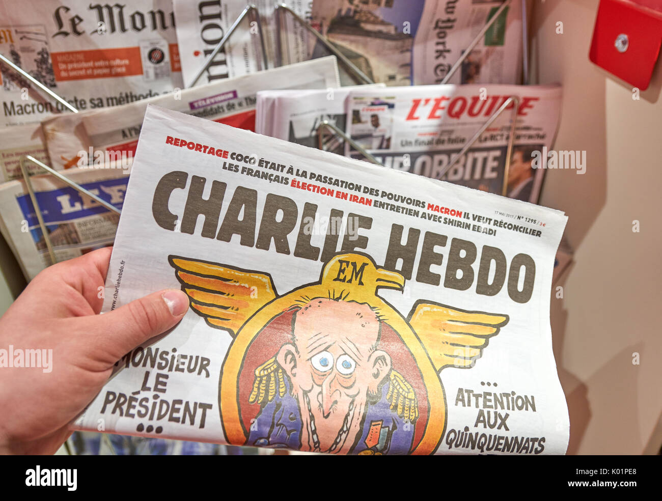 PARIS, ENGLAND - MAY 14, 2017 : A hand holding Charlie Hebdo over newsstand background in Paris. Charlie Hebdo is a French satirical weekly magazine,  Stock Photo