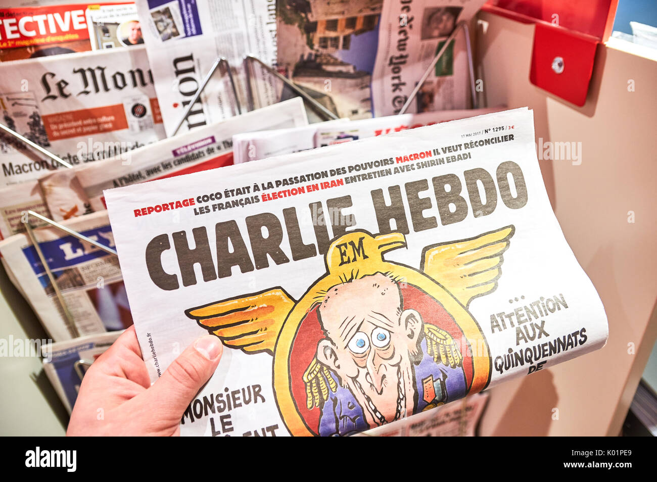 PARIS, ENGLAND - MAY 14, 2017 : A hand holding Charlie Hebdo over newsstand background in Paris. Charlie Hebdo is a French satirical weekly magazine,  Stock Photo