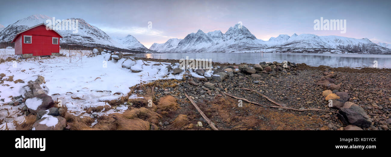 Panorama of the wooden hut called Rorbu framed by frozen sea and snowy peaks Svensby Lyngen Alps Tromsø Norway Europe Stock Photo