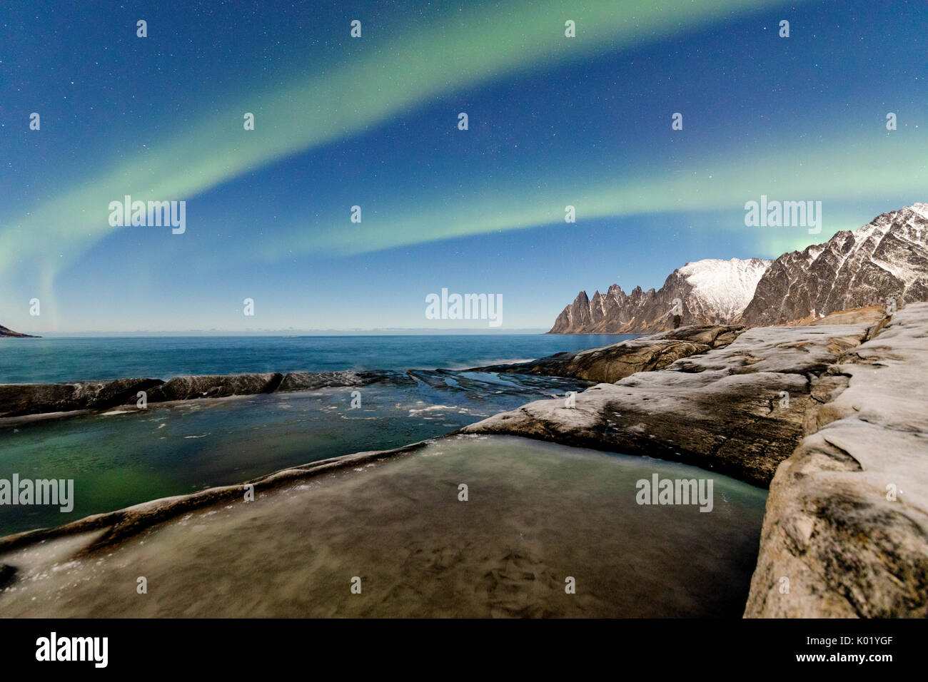 The Northern Lights and stars illuminate the rocky peaks and icy sea Tungeneset Senja Tromsø Norway Europe Stock Photo