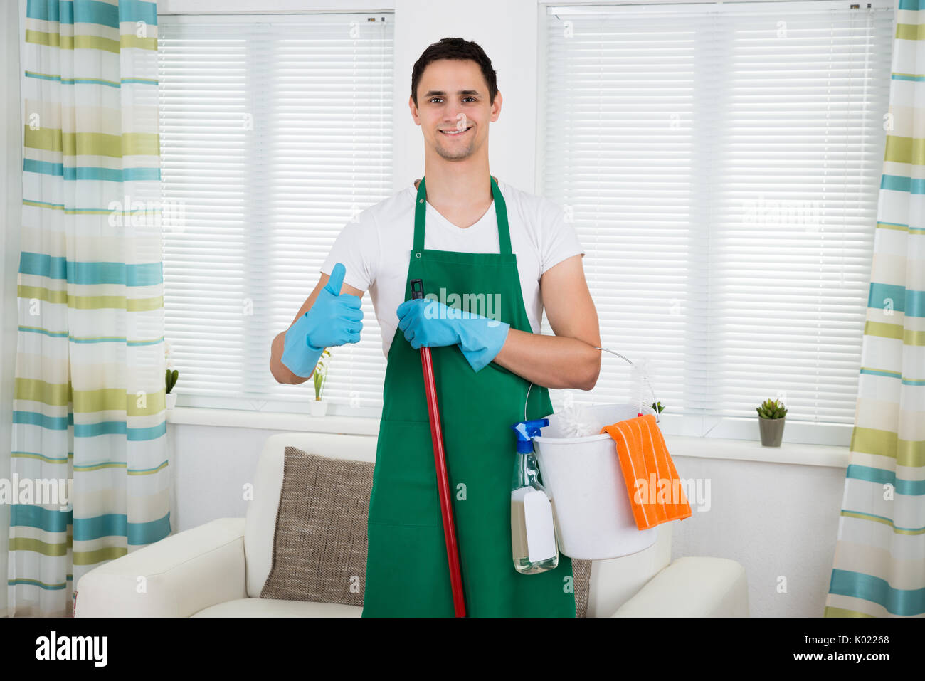 Portrait of happy male cleaner gesturing thumbs up while standing at home Stock Photo