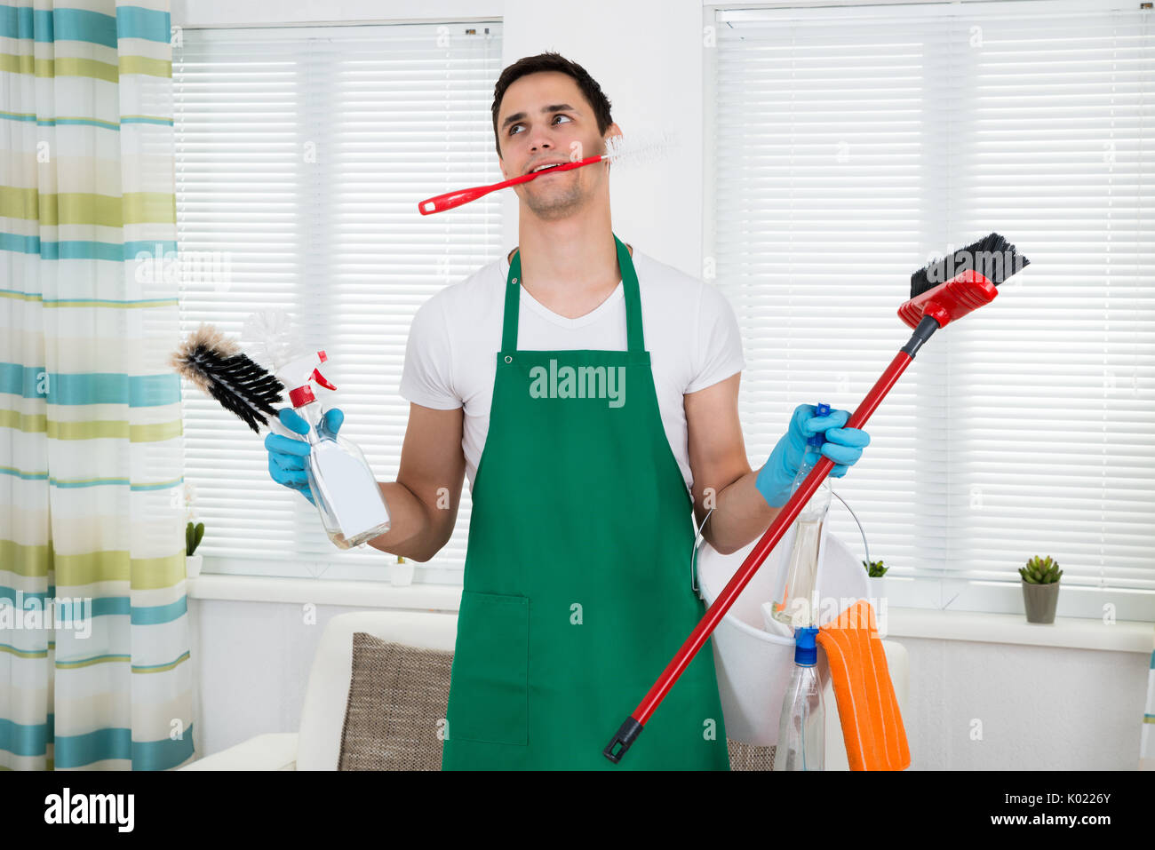 Overburdened cleaner holding various cleaning equipment at home Stock Photo