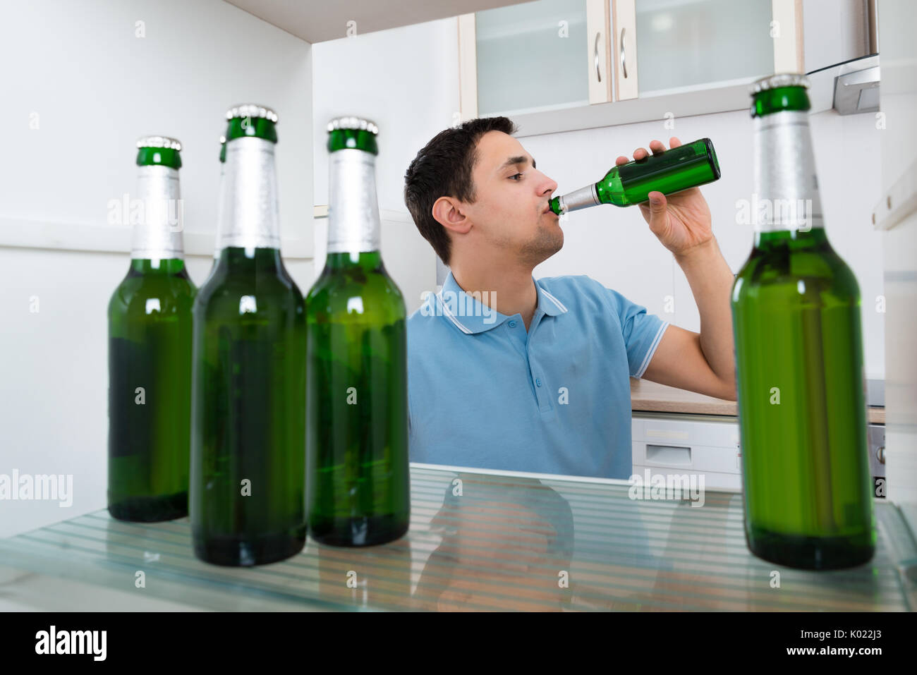 Young man drinking beer while standing in front of refrigerator at home Stock Photo