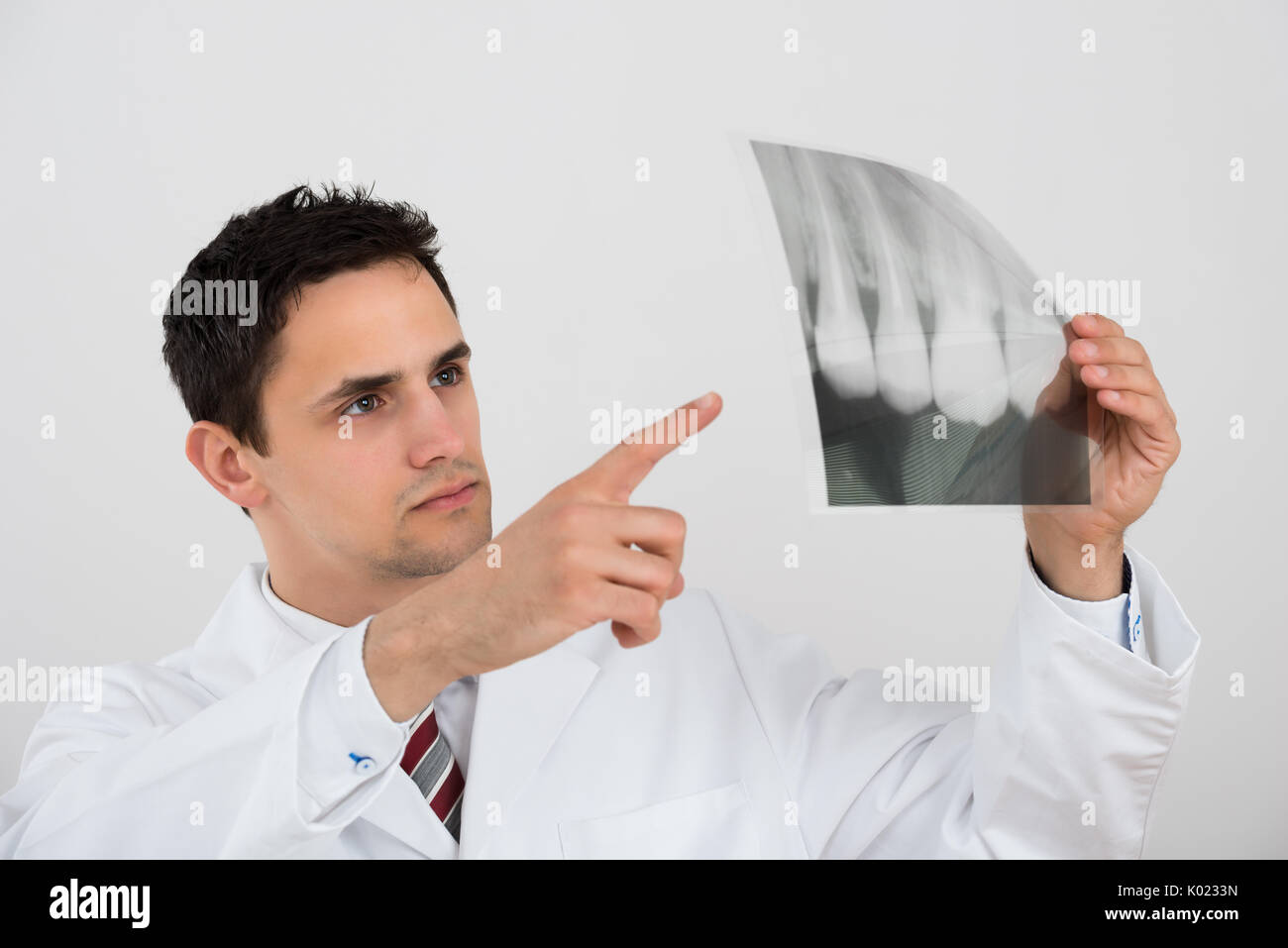 Young male dentist examining dental xray against white background Stock Photo