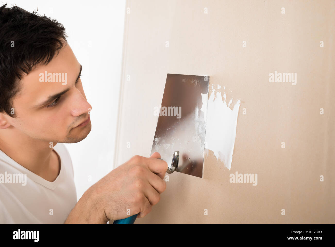 Young man using putty knife on white wall at home Stock Photo