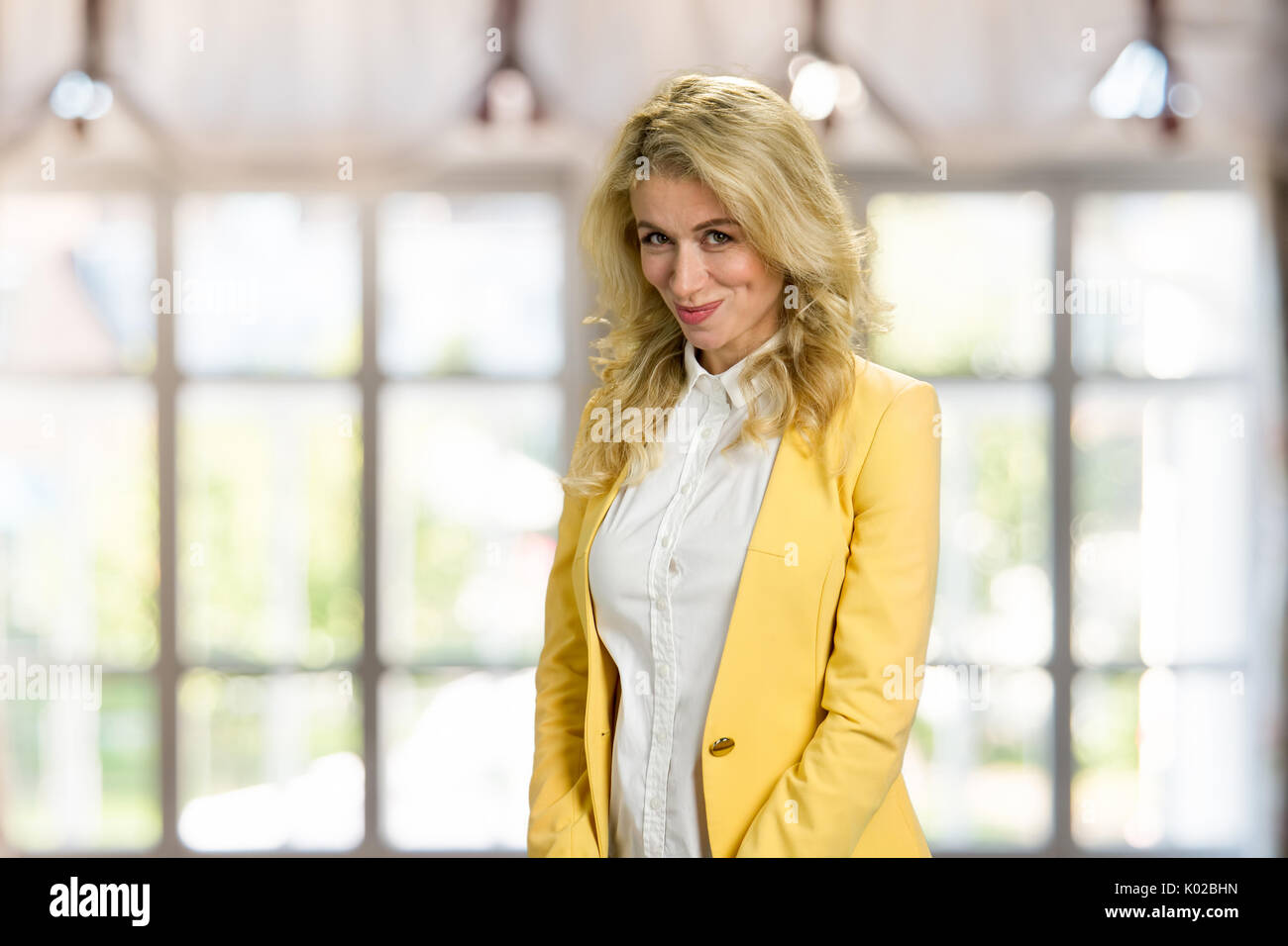 Beautiful shy girl looking at camera. Beautiful embarrassed blonde woman in formal wear posing on blurred background. Stock Photo