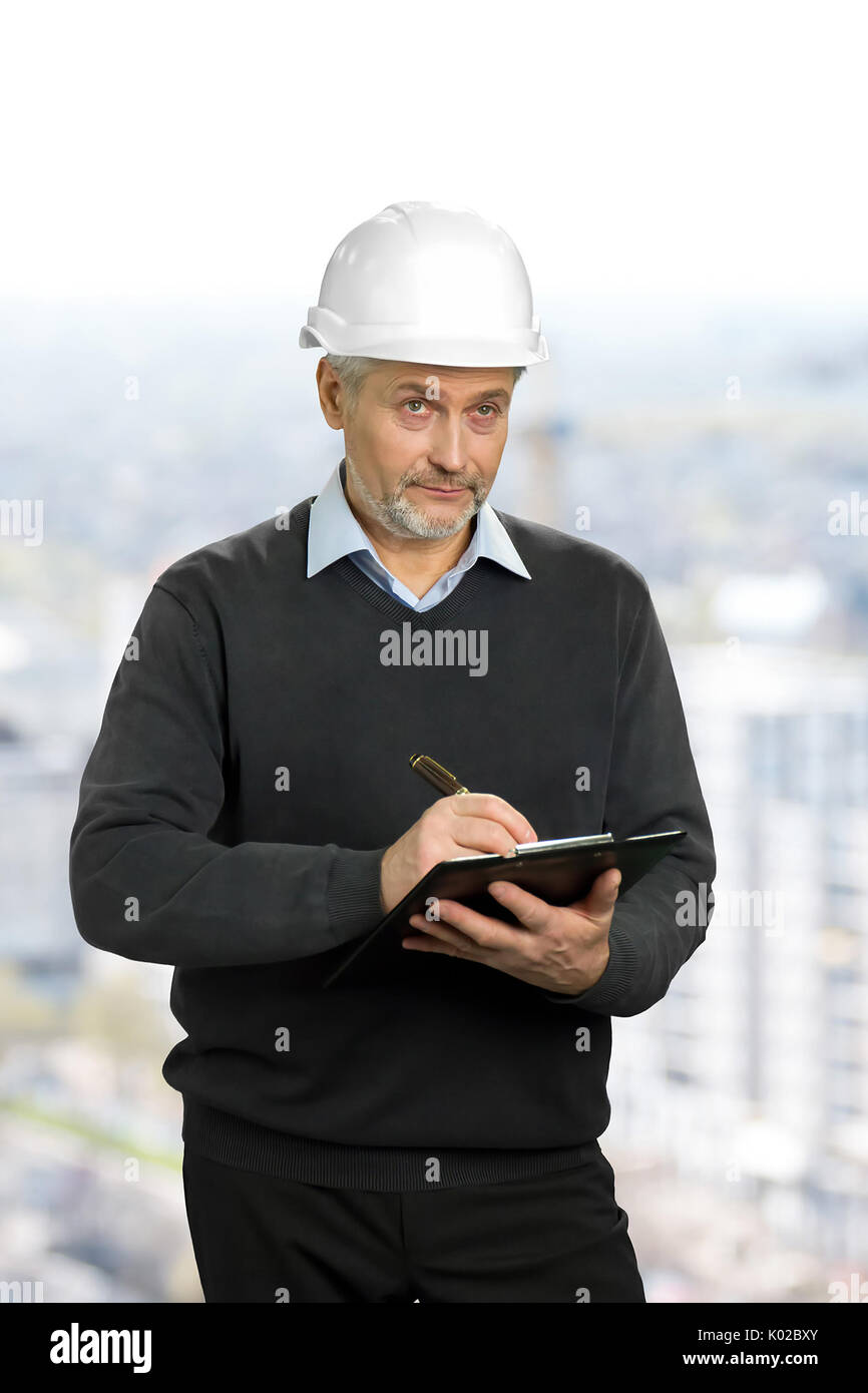 Mature architect looking on object. Elderly engineer in safety helmet