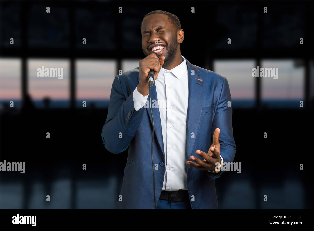 Singing man on the evening background. Darkskinned man with microphone. Black man is singing with closed eyes and passion. Stock Photo