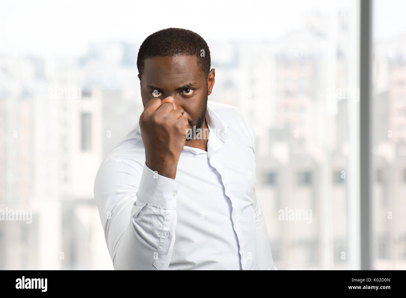 Serious man holding out his fist. Black man in white shirt shake his fist. Concept of power and authority. Stock Photo