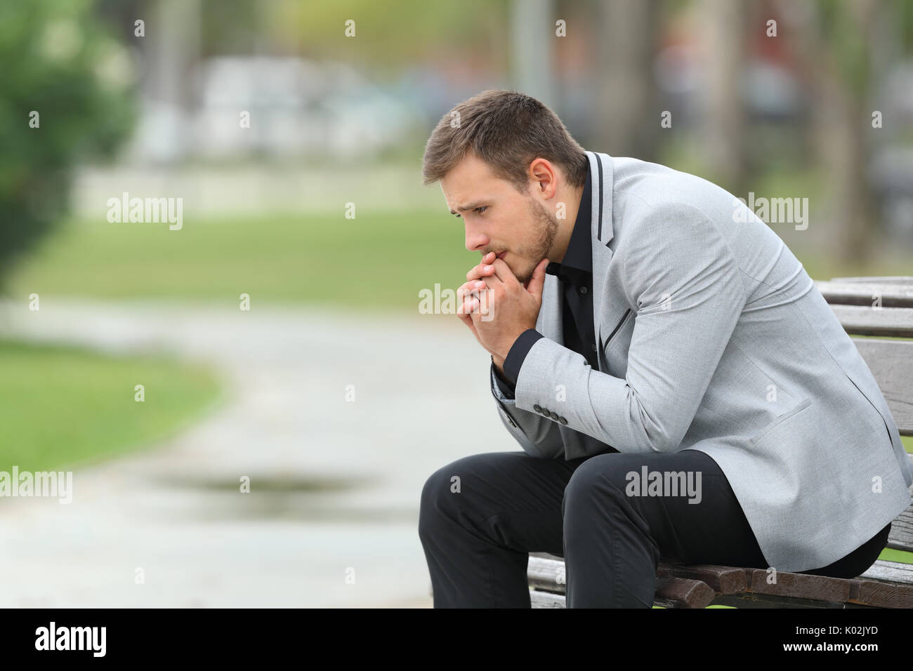 Side view portrait of a worried businessman sitting on a bench in a park Stock Photo