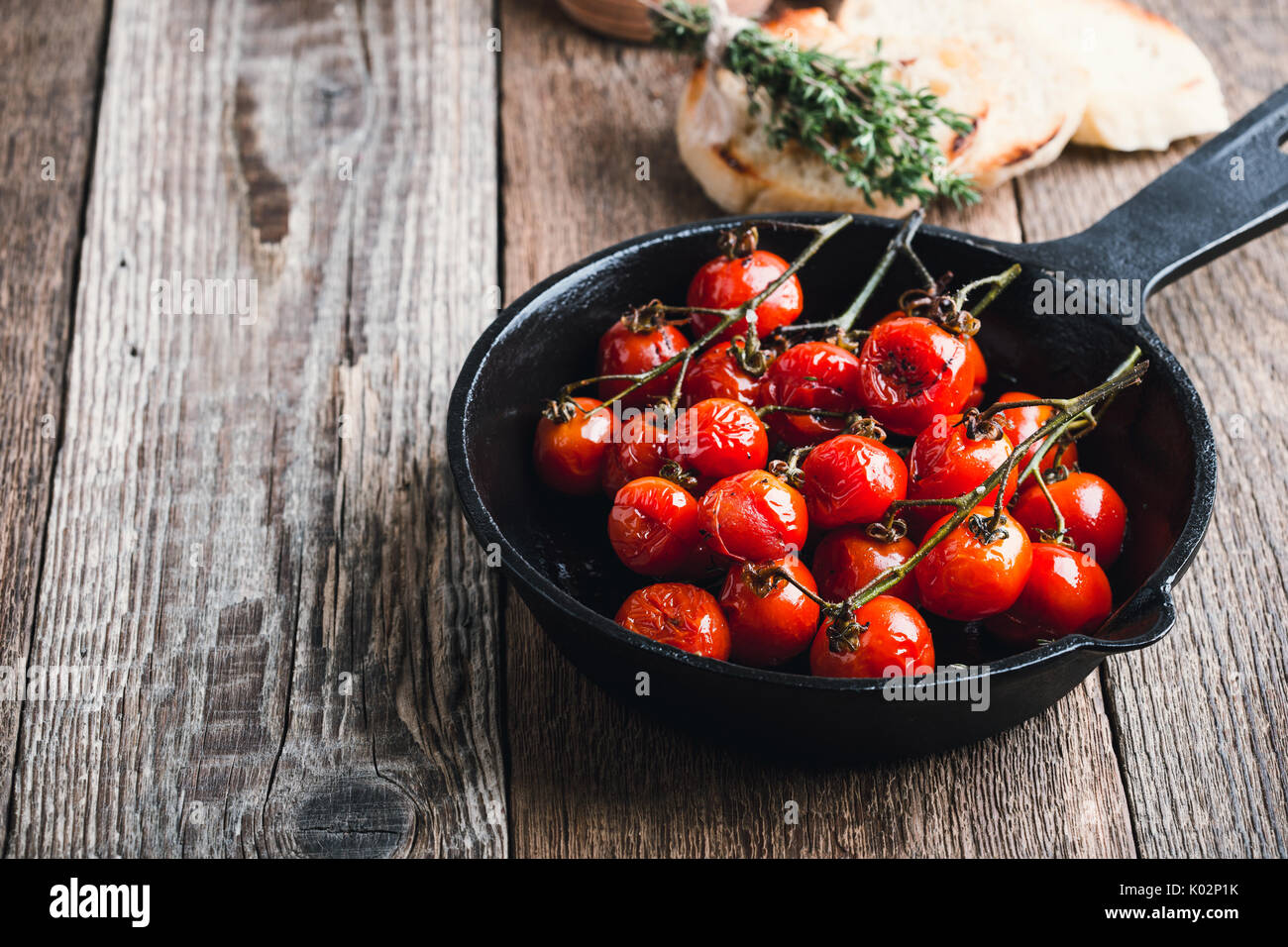 Roasted cherry tomatoes in cast iron skillet on rustic wooden board